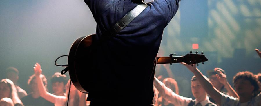 Man on stage with a guitar leading musical worship